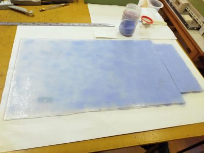 板ガラスの上にオパールセントガラスの粉（白と青）をふるいで載せて、色ガラスを作ります